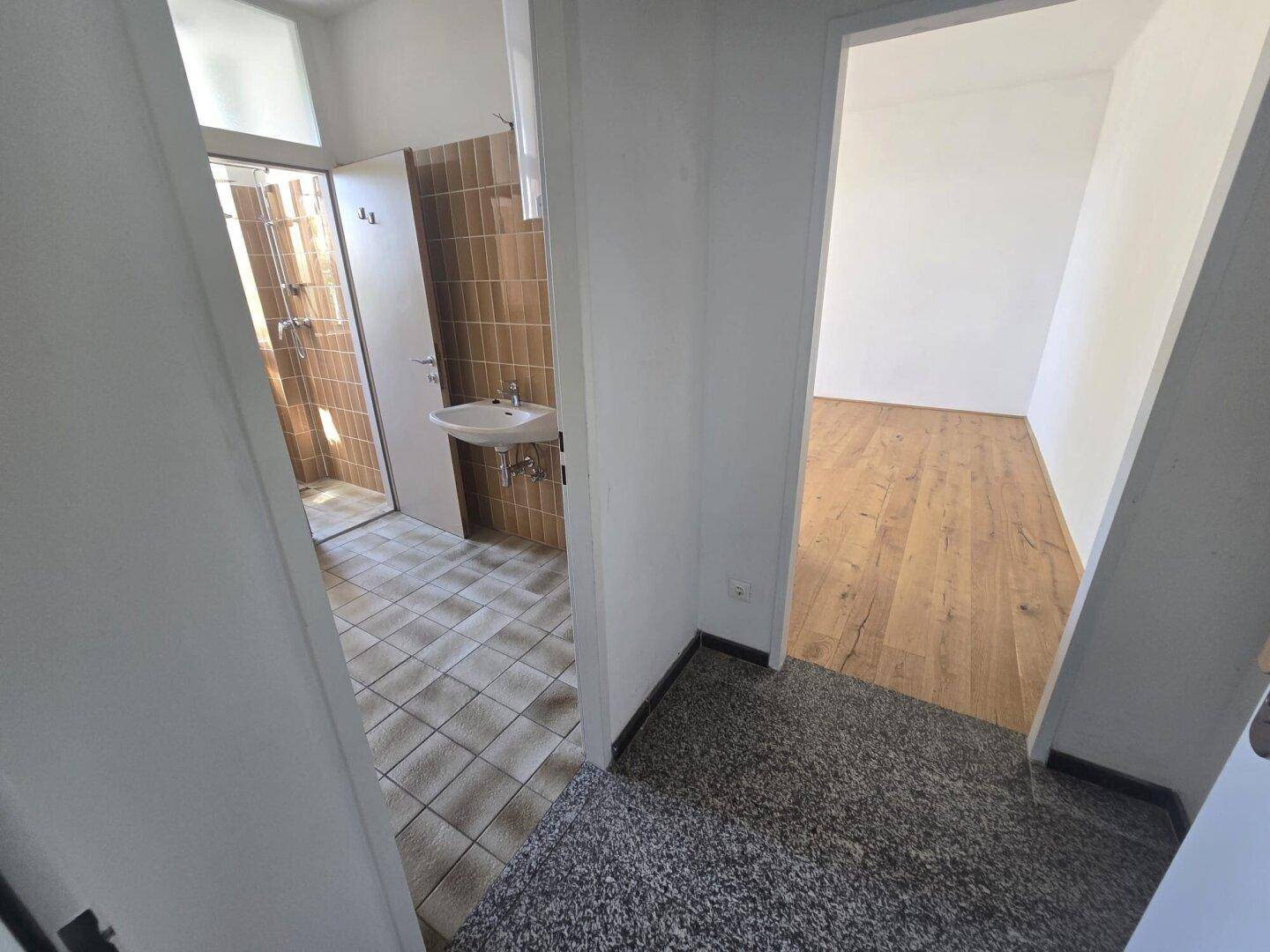 Flur mit Teppichboden, der zu einem Badezimmer mit braunen Fliesen führt.