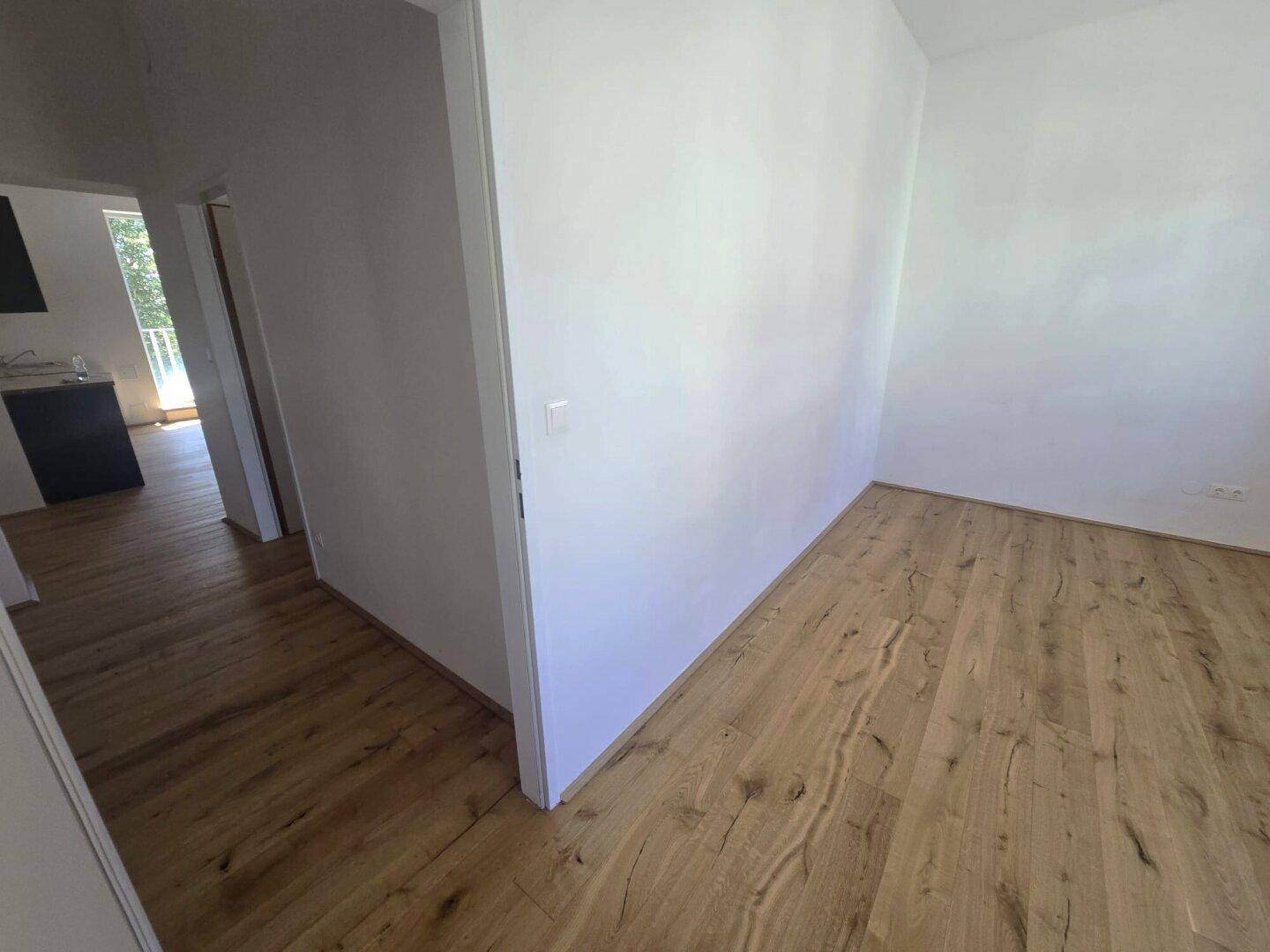 Heller Raum mit Holzboden und weiß gestrichenen Wänden, mit Blick in einen weiteren Bereich.