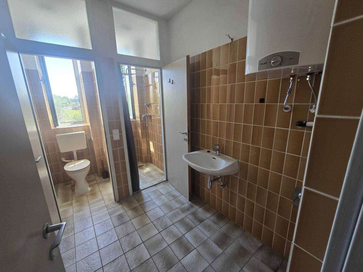 Badezimmer mit braunen Wand- und Bodenfliesen, ausgestattet mit Dusche und WC.
