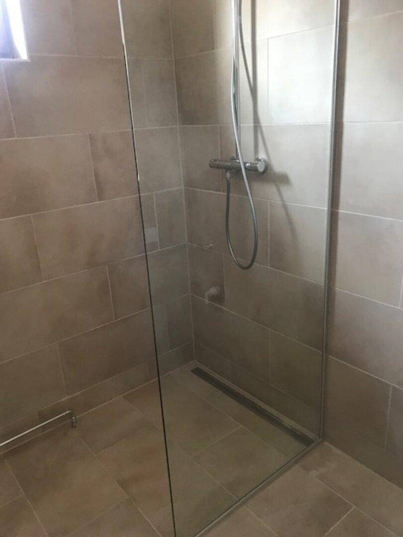 Duschbereich mit modernen grauen Fliesen und Glasabtrennung in einem Badezimmer.