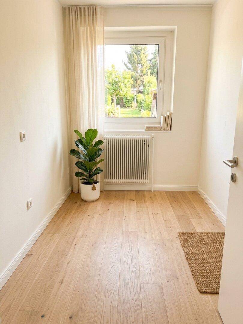 Helles Zimmer mit Holzfußboden, großem Fenster und Heizkörper, bereit zur Einrichtung.