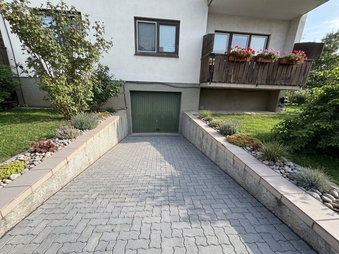 Zufahrt zur Tiefgarage mit gepflastertem Weg und bepflanzten Böschungen am Gebäude.