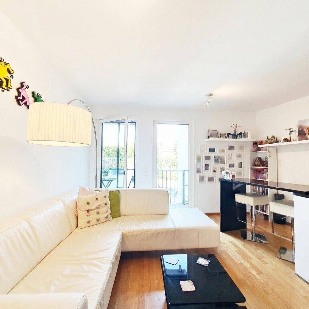 Heller Wohnbereich mit bequemer Couch, Holzboden und Zugang zum Balkon.