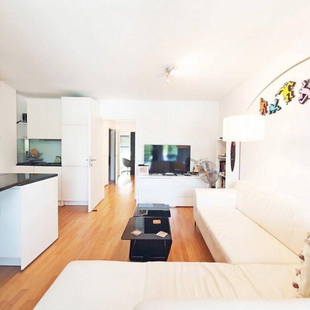 Geräumiger Wohnbereich mit Sofa, Fernseher und offener Verbindung zur Küche.