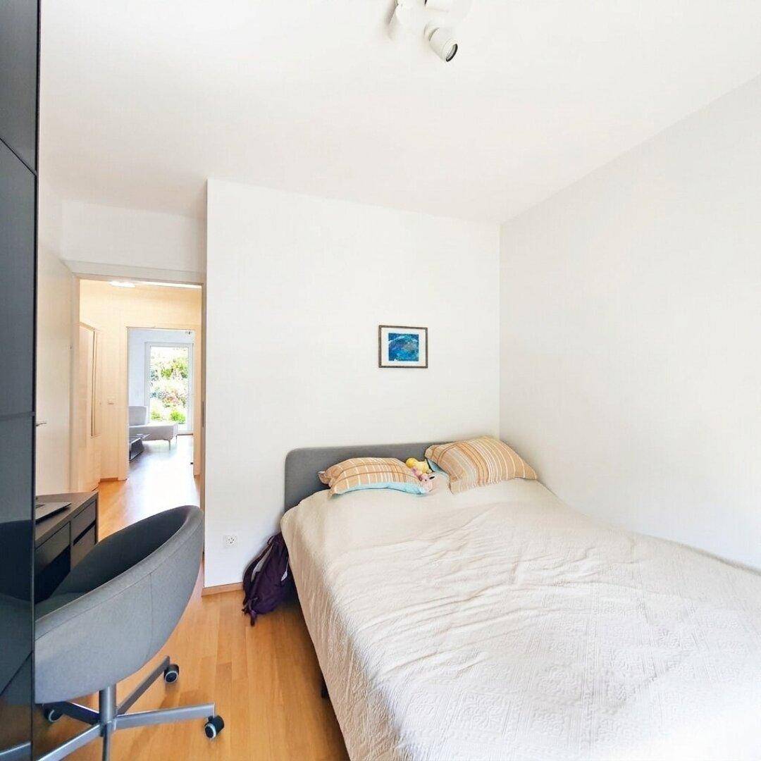 Schlafzimmer mit Bett, Schreibtisch und Holzboden, bietet eine ruhige Arbeitsumgebung.