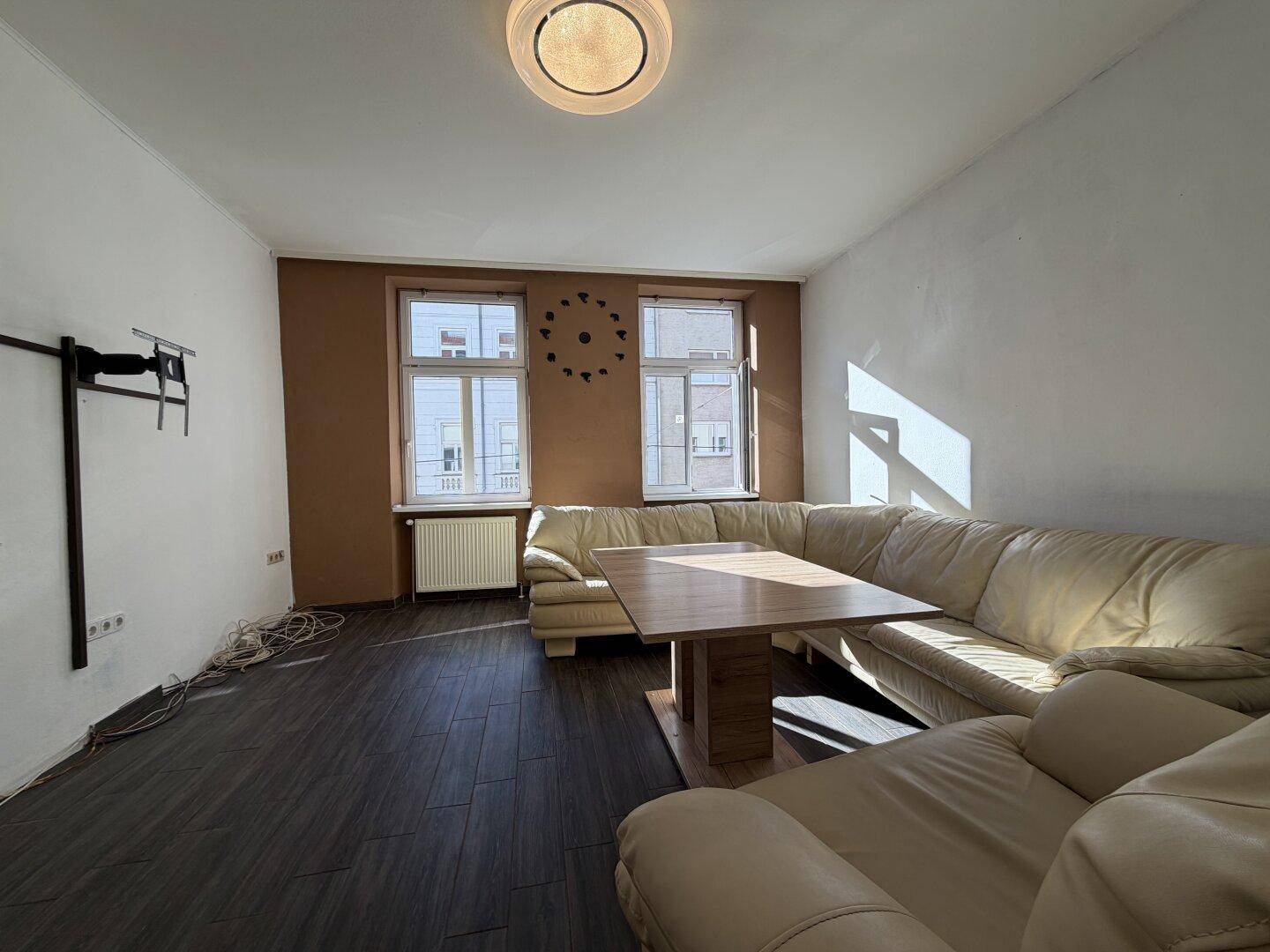 Gemütliches Wohnzimmer mit großem beigem Ecksofa, Holztisch und dunklem Laminatboden.
