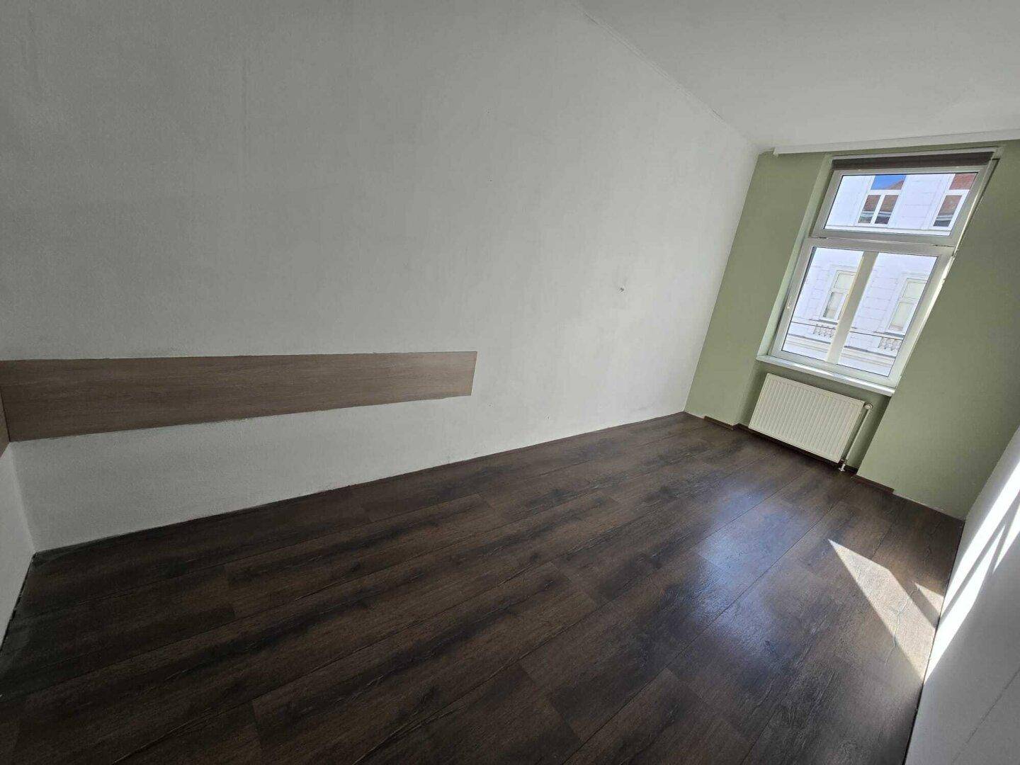 Leeres Zimmer mit dunklem Laminatboden, einer hellgrünen Akzentwand und einem dekorativen Holzpaneel.