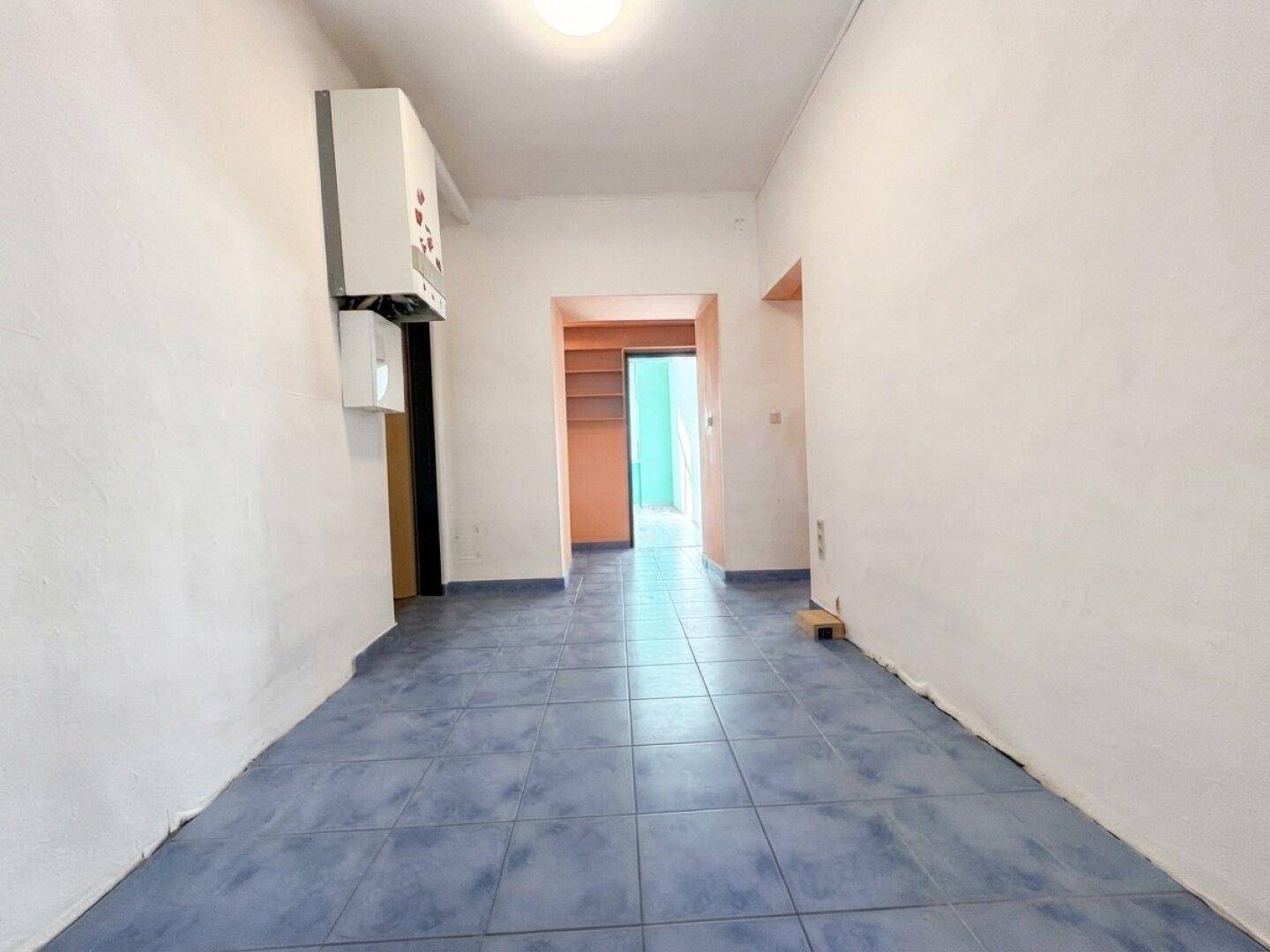 Flur mit blauen Fliesen und einem an der Wand montierten Warmwasserbereiter, der zu weiteren Räumen führt.