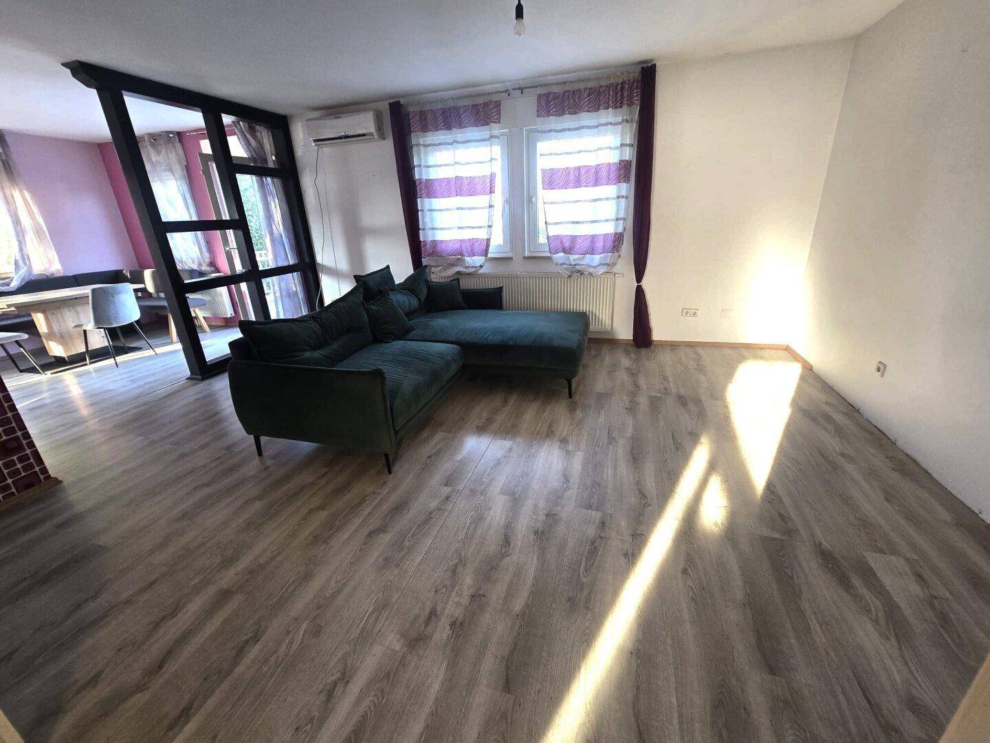 Geräumiges Wohnzimmer mit Laminatboden und bequemer Eckcouch, hell und einladend.