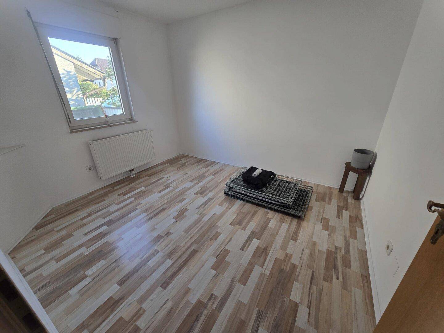 Helles Schlafzimmer mit Laminatboden und großem Fenster, bereit zur individuellen Gestaltung.
