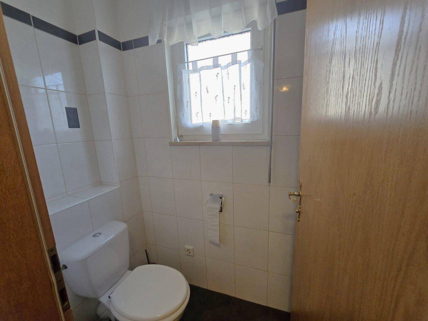 Separates WC mit Fenster und weißen Fliesen, praktisch und hell.