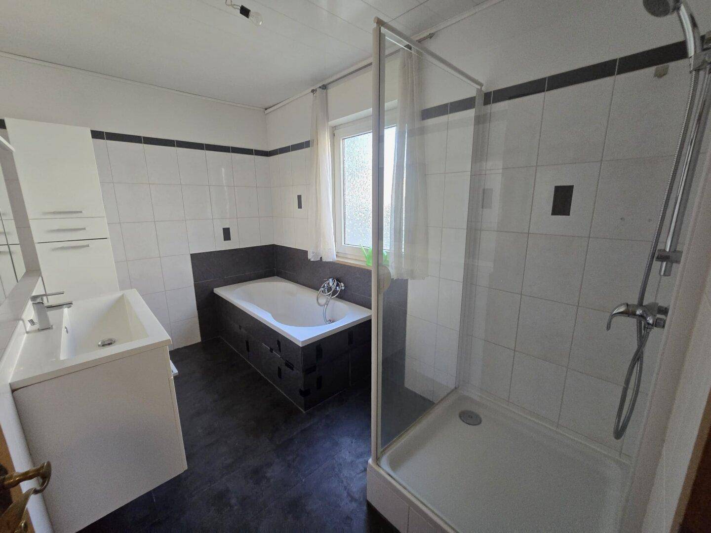 Badezimmer mit Badewanne, Duschkabine, Einzelwaschbecken und Fenster.