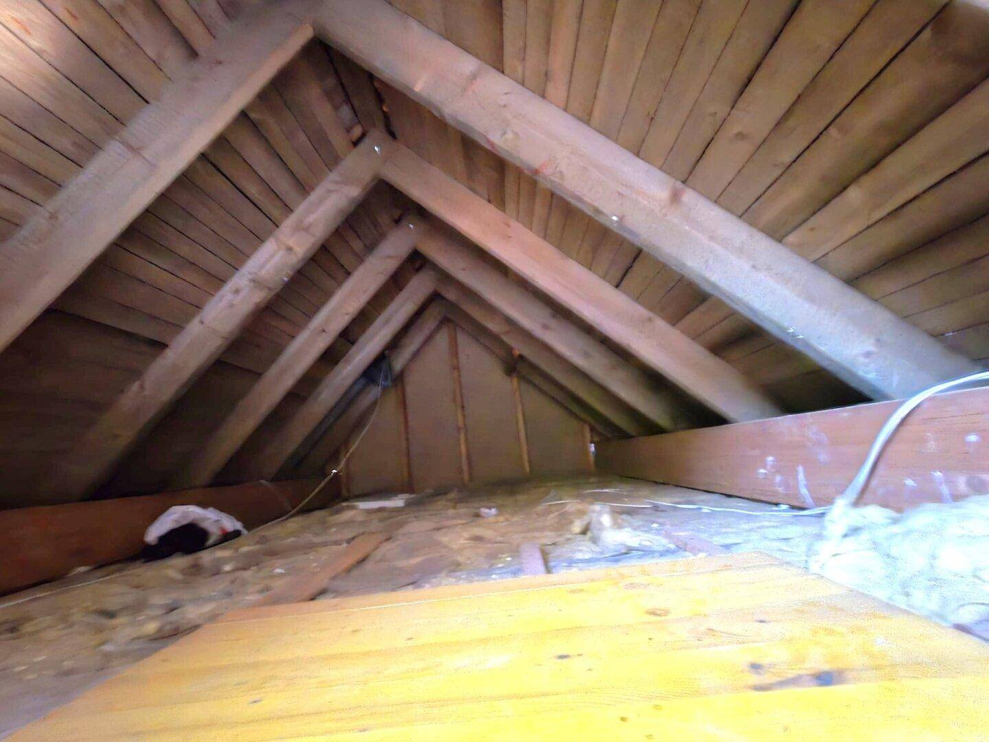 Unausgebauter Dachboden mit sichtbaren Holzbalken und Dämmmaterial.
