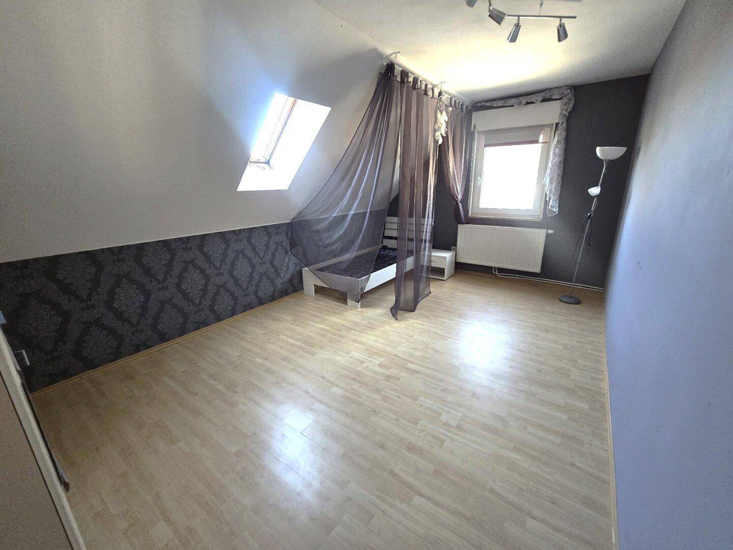 Schlafzimmer im Dachgeschoss mit Laminatboden, Dachfenster und dekorativer Tapete.