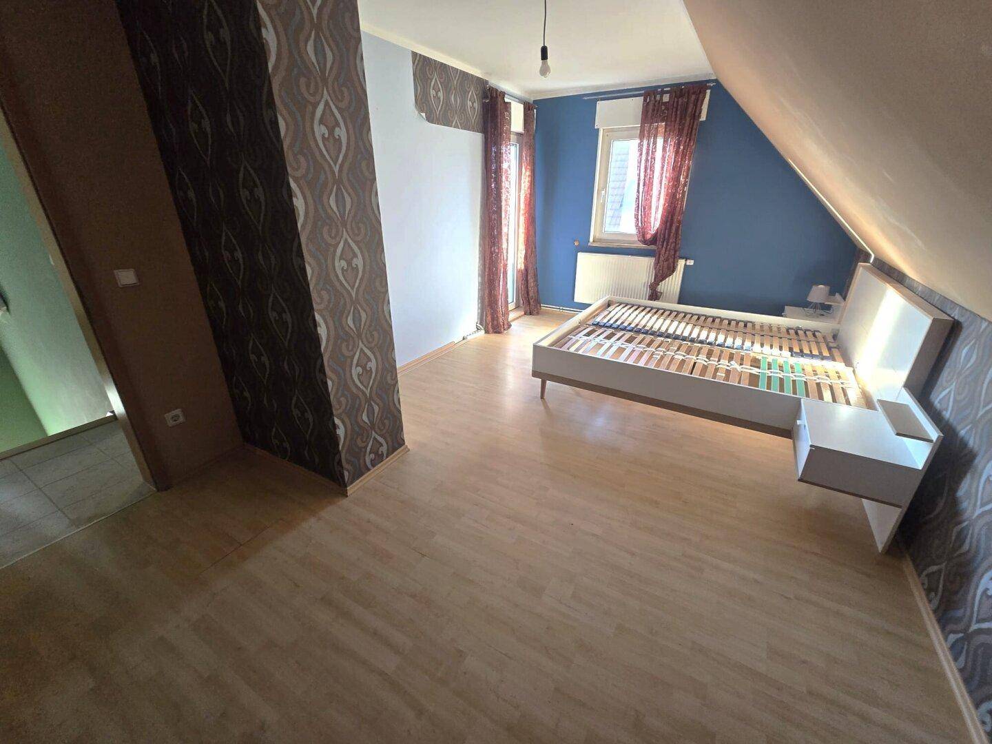 Geräumiges Schlafzimmer im Dachgeschoss mit Laminatboden und farbigen Wänden.