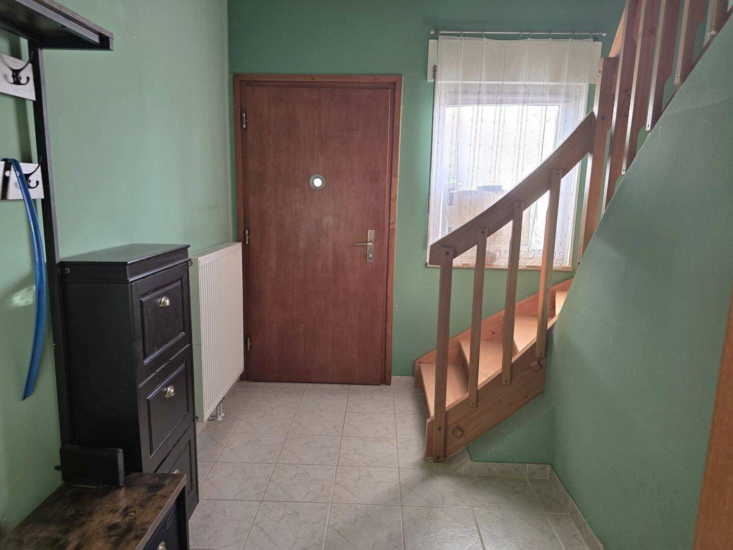 Eingangsbereich mit Fliesenboden, Garderobe und Holztreppe zum Obergeschoss.