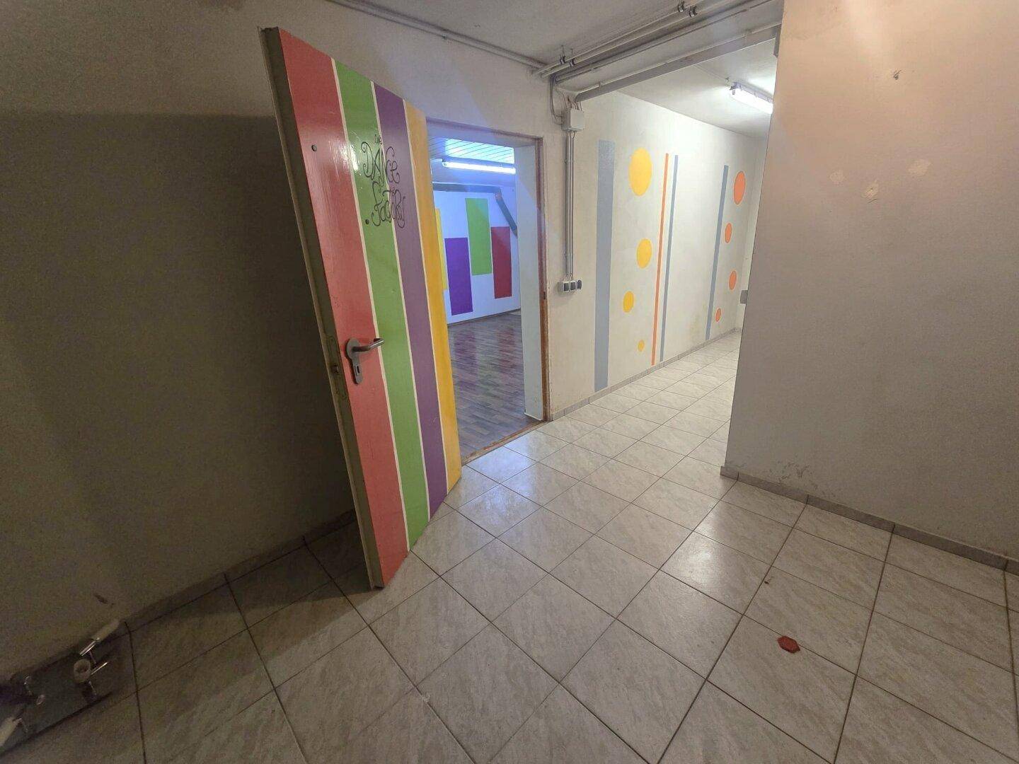 Kellerflur mit Fliesenboden und farbenfroher Wandgestaltung, führt zu weiteren Räumen.