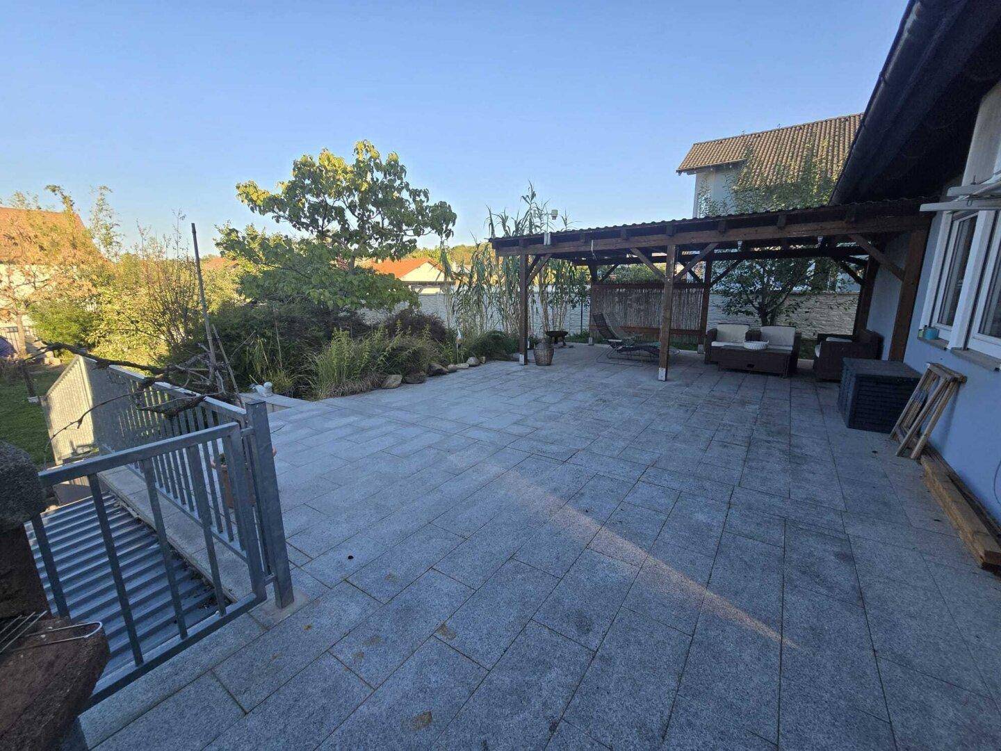 Große gepflasterte Terrasse mit Pergola und Sitzgelegenheiten im Freien.