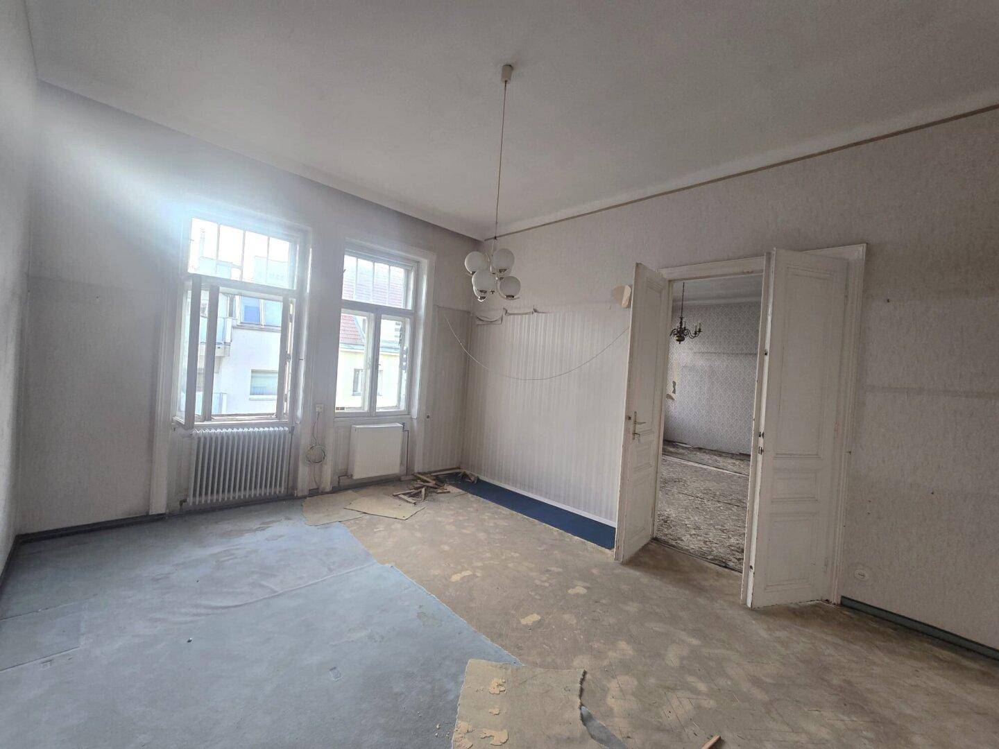 Leeres Zimmer mit zwei Fenstern und teilweise entfernter Tapete, bereit zur Renovierung.