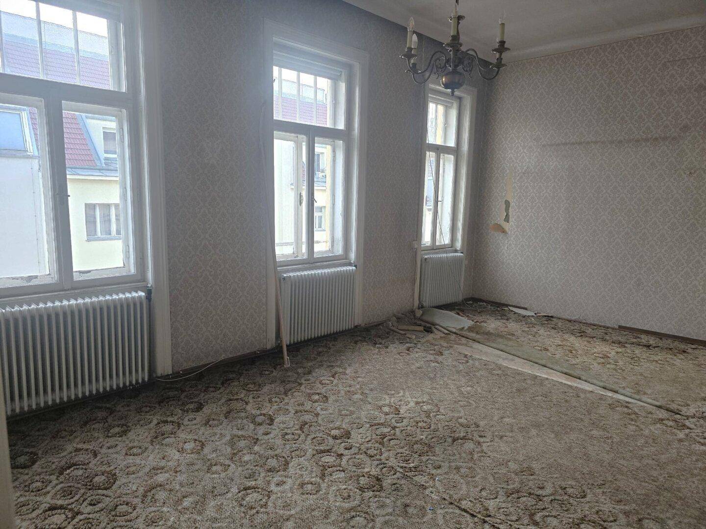 Helles Wohnzimmer mit altem Teppichboden und Tapeten, bereit für eine Modernisierung.