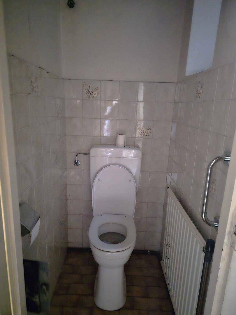 Kleines WC mit weißen Fliesen, Toilette und Heizkörper, funktional und einfach gehalten.