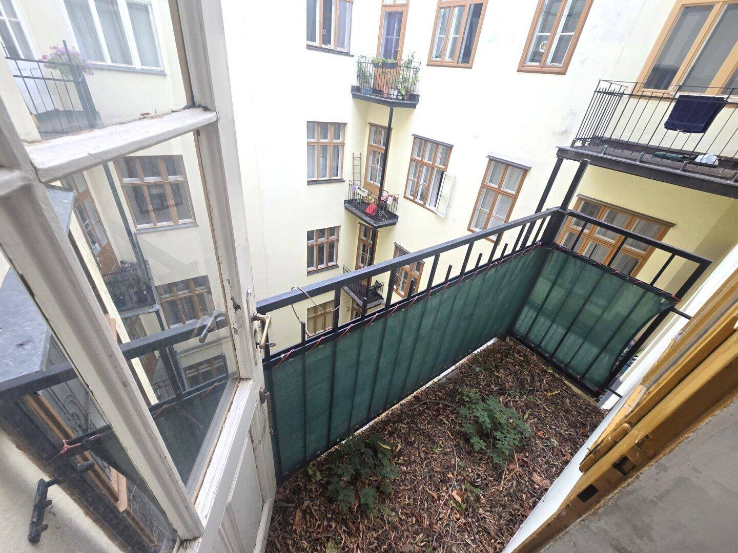 Kleiner Balkon mit Blick in den Innenhof, umgeben von weiteren Gebäuden und viel Tageslicht.