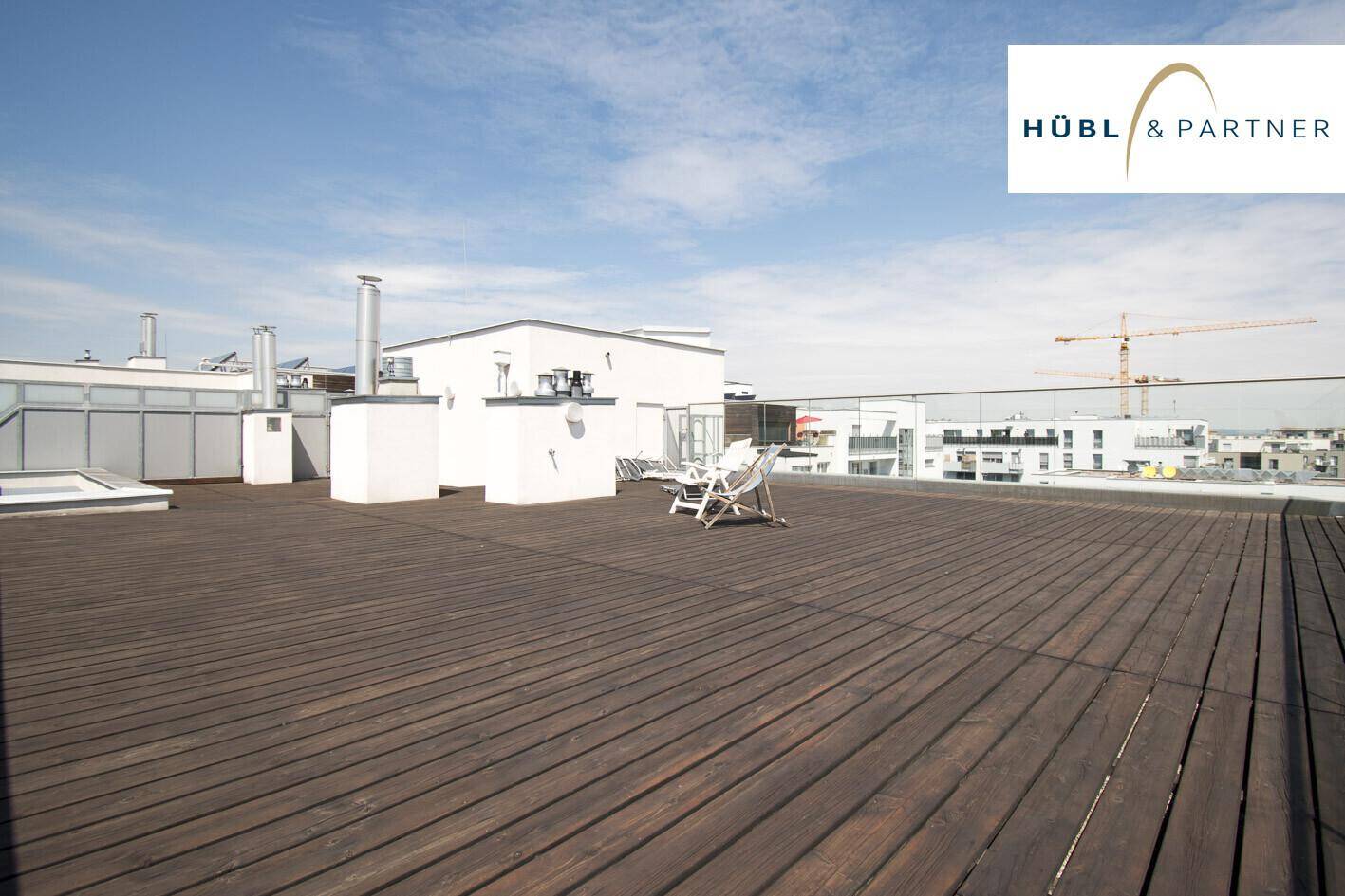 Geräumige Dachterrasse mit Holzbelag und Liegestühlen, bietet einen weiten Blick über die Stadt.