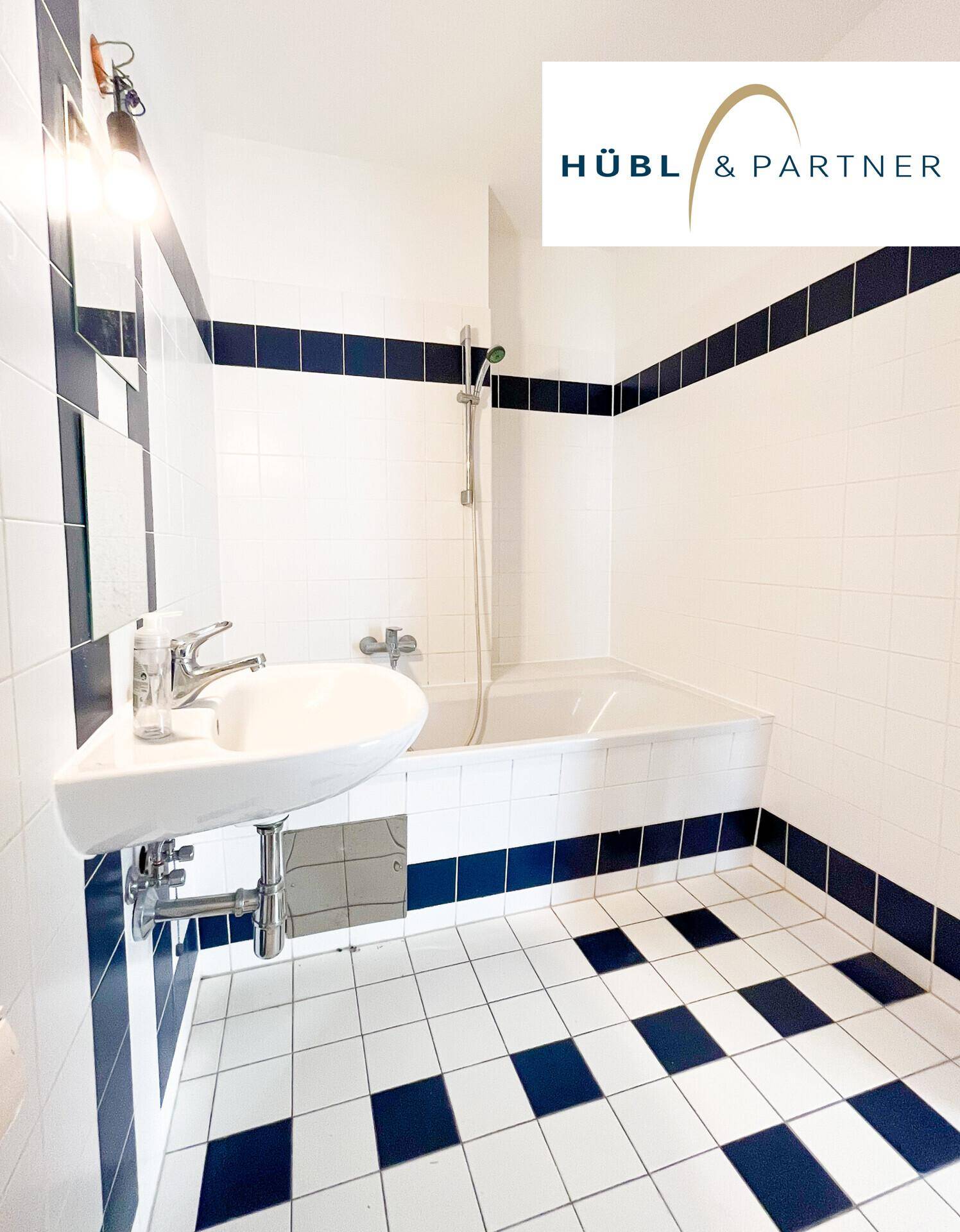 Badezimmer mit weiß-blauen Fliesen, Waschbecken und Dusch-Badewannen-Kombination.