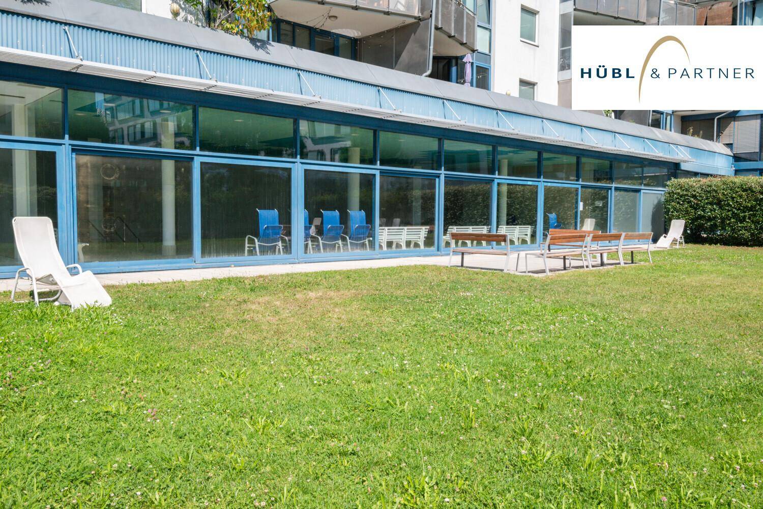 Gepflegte Rasenfläche vor einem Gebäude mit großen Glasfronten, ideal zum Entspannen.