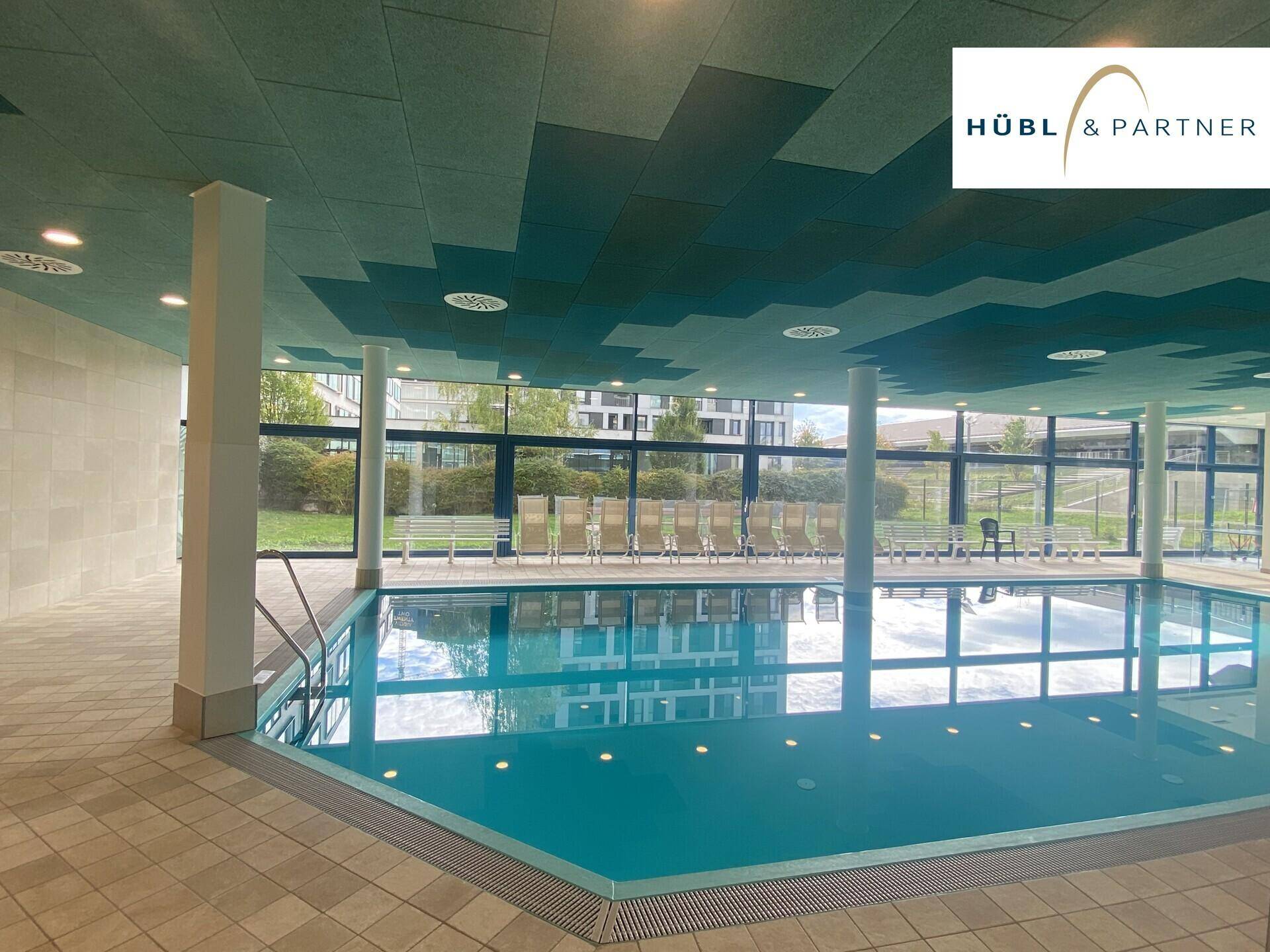 Modernes Hallenbad mit großem Schwimmbecken und viel Tageslicht durch die Fensterfront.