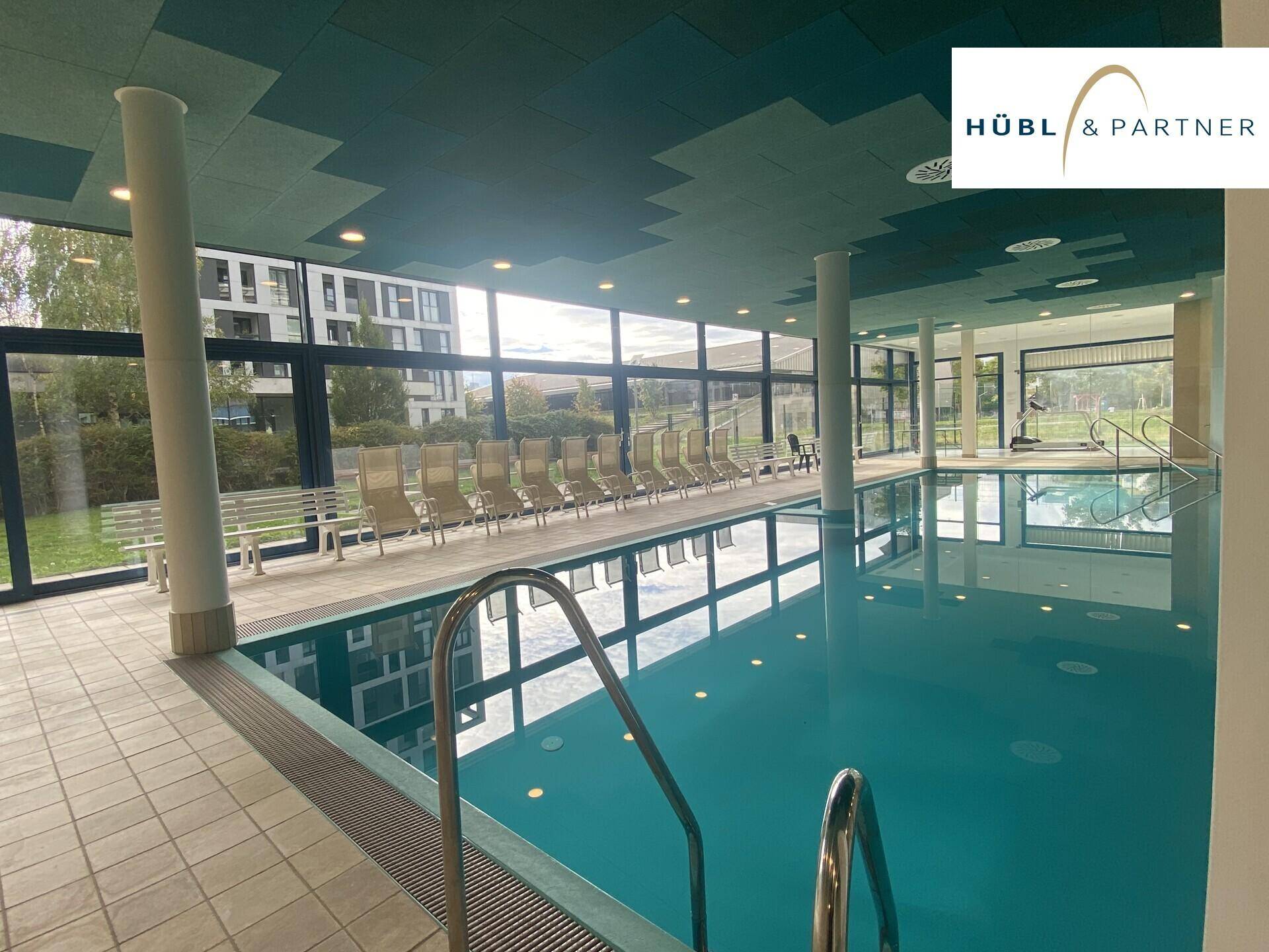 Großzügiges Hallenbad mit Schwimmbecken und Liegebereich, umgeben von großen Fenstern.