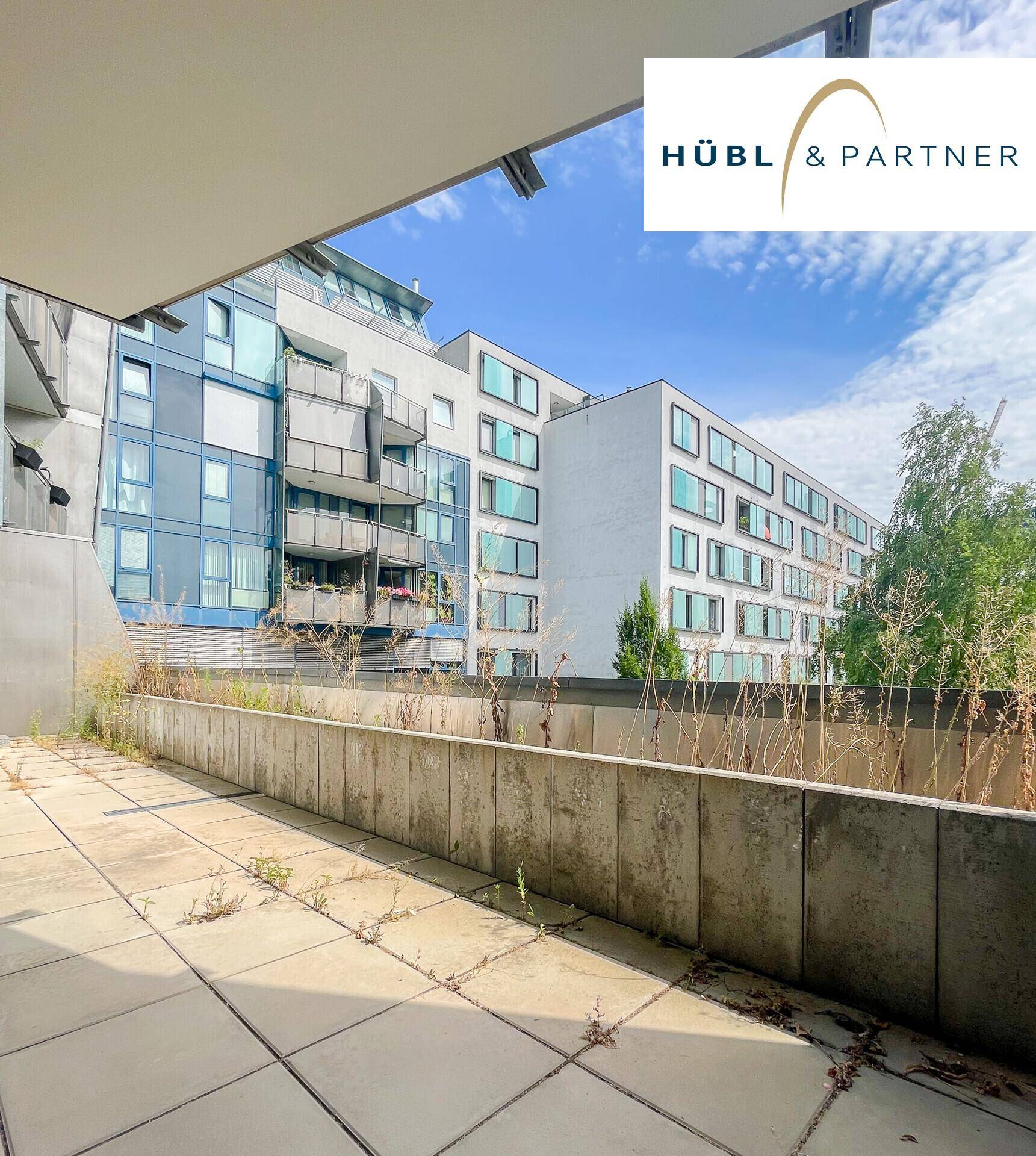 Große Terrasse mit Betonplatten und Blick auf moderne Wohngebäude in der Umgebung.