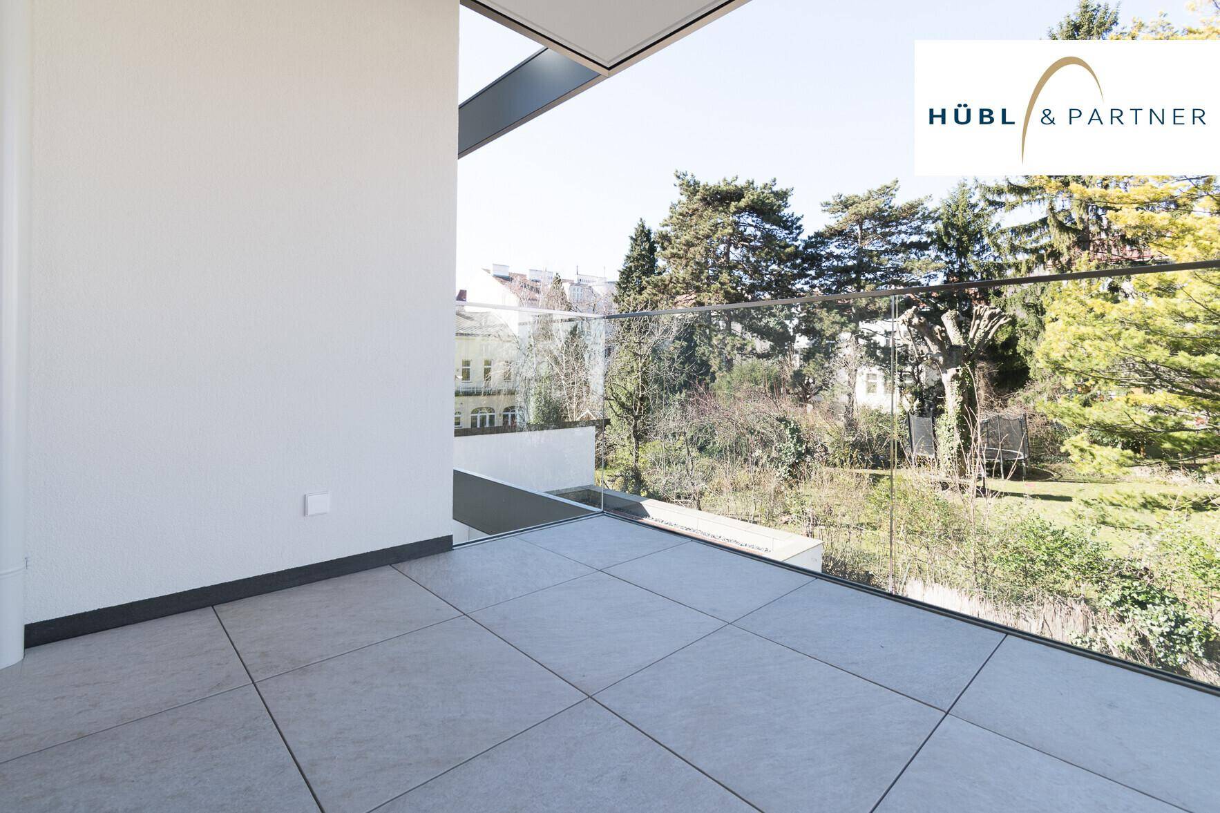 Moderner Balkon mit Glasgeländer und Fliesenboden bietet einen weiten Blick ins Grüne.