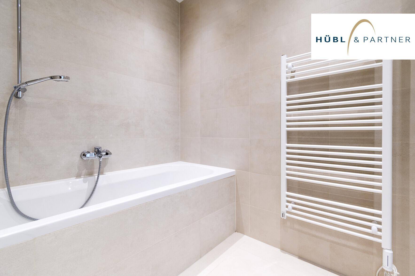 Modernes Badezimmer mit Badewanne, beigefarbenen Fliesen und beheiztem Handtuchhalter.