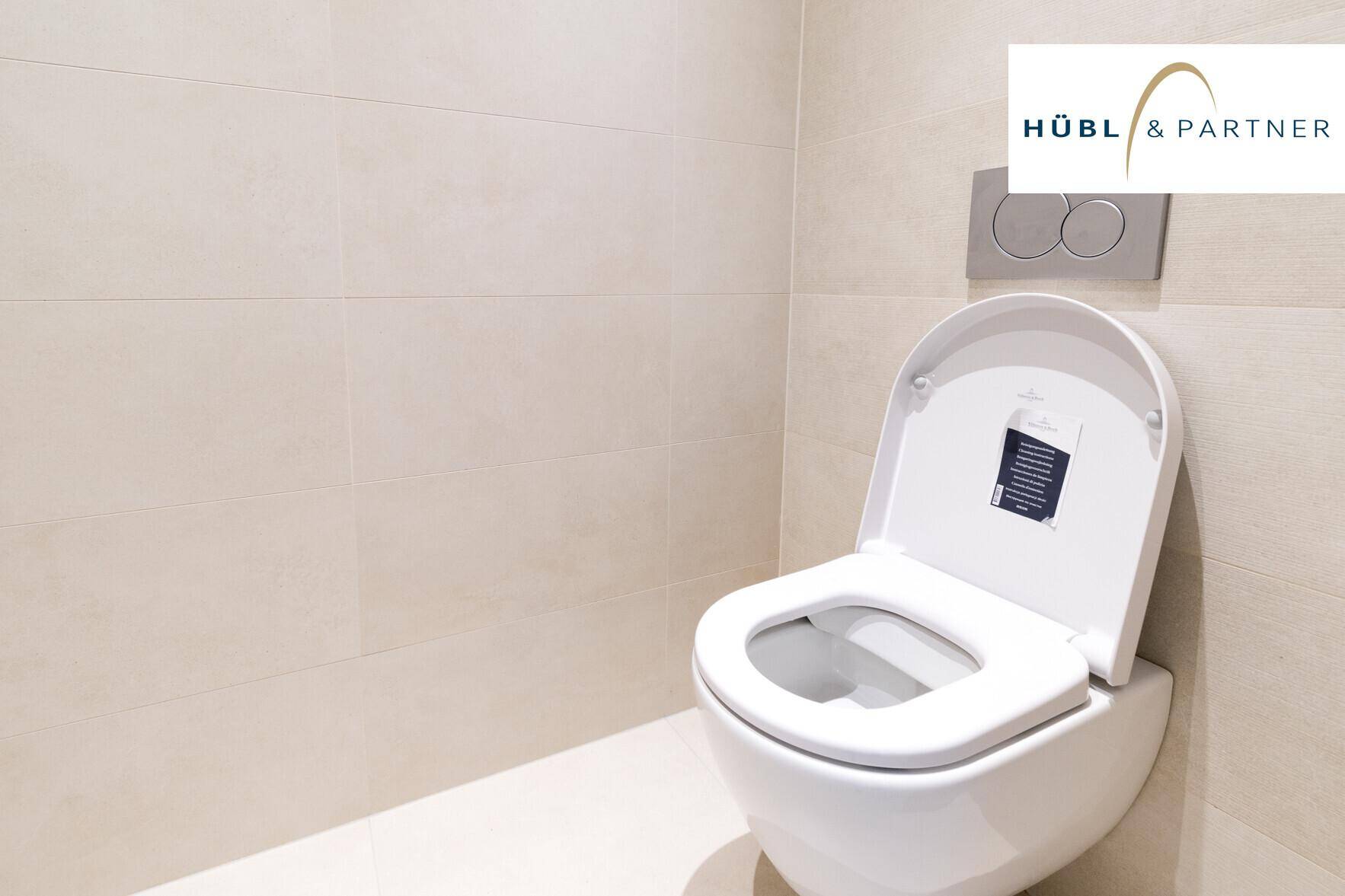 Separates WC mit wandmontierter Toilette und beigefarbenen Fliesen, in modernem Design.