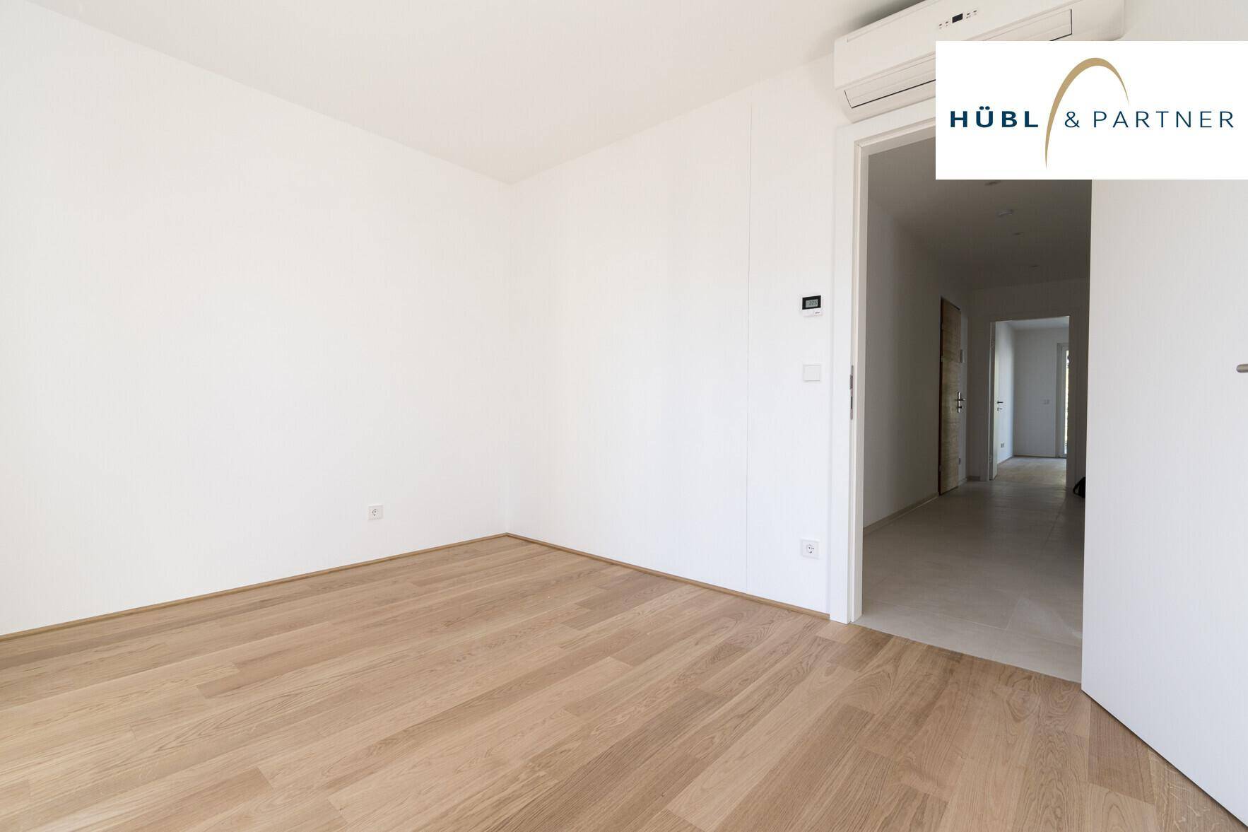 Leeres Schlafzimmer mit Parkettboden und Klimaanlage, bereit für die individuelle Einrichtung.