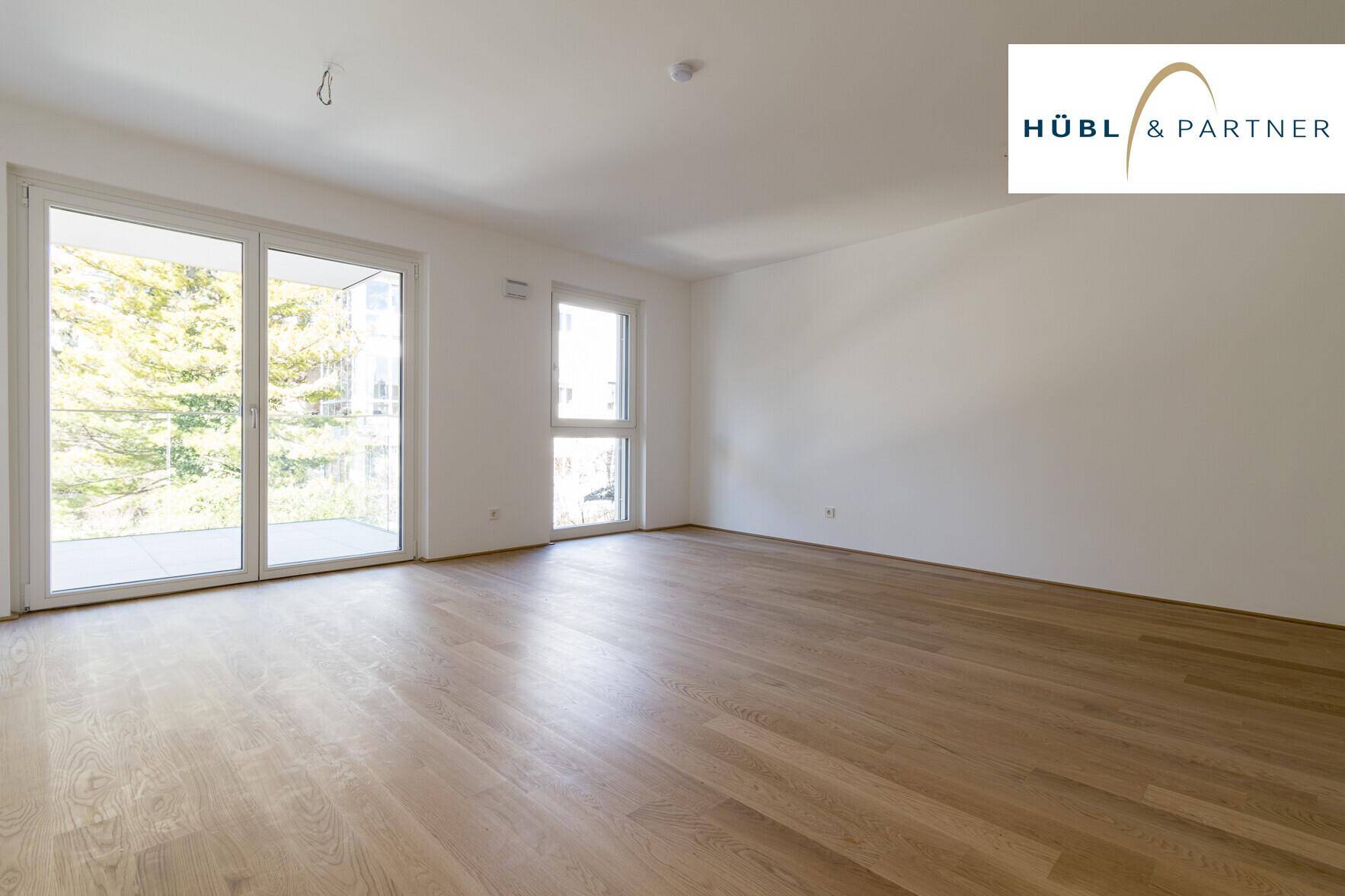 Helles, leeres Wohnzimmer mit neuem Parkettboden und Zugang zu einem Balkon.