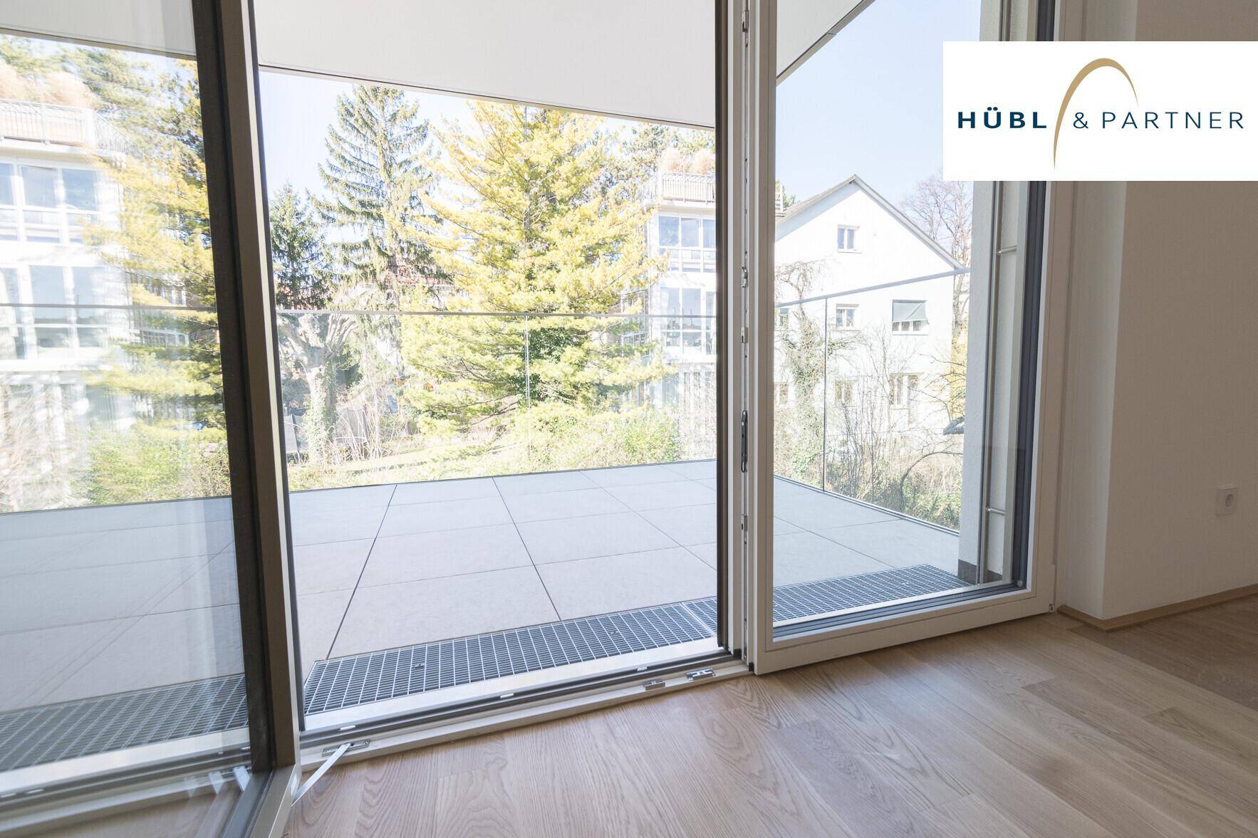 Große Schiebetüren im Wohnzimmer bieten direkten Zugang zu einem gefliesten Balkon mit Grünblick.