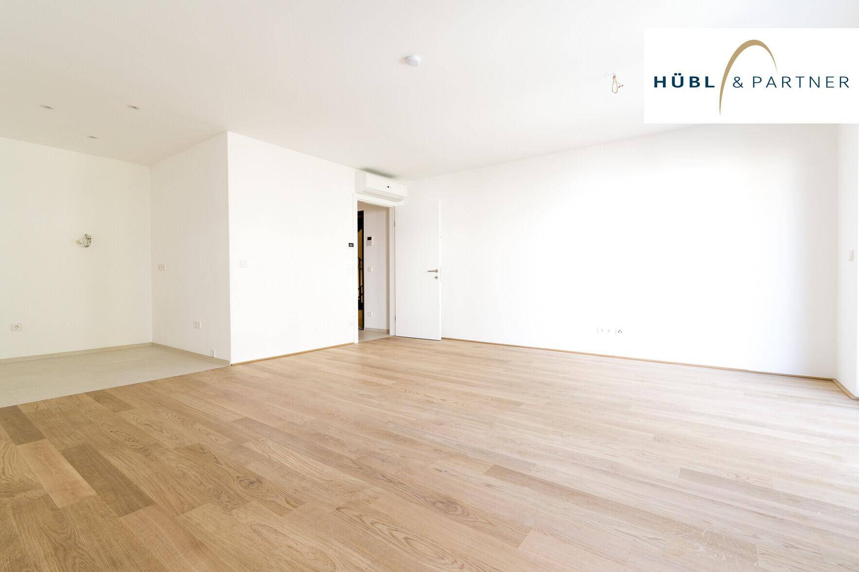 Geräumiges, helles Wohnzimmer mit Parkettboden und einem Bereich für eine offene Küche.