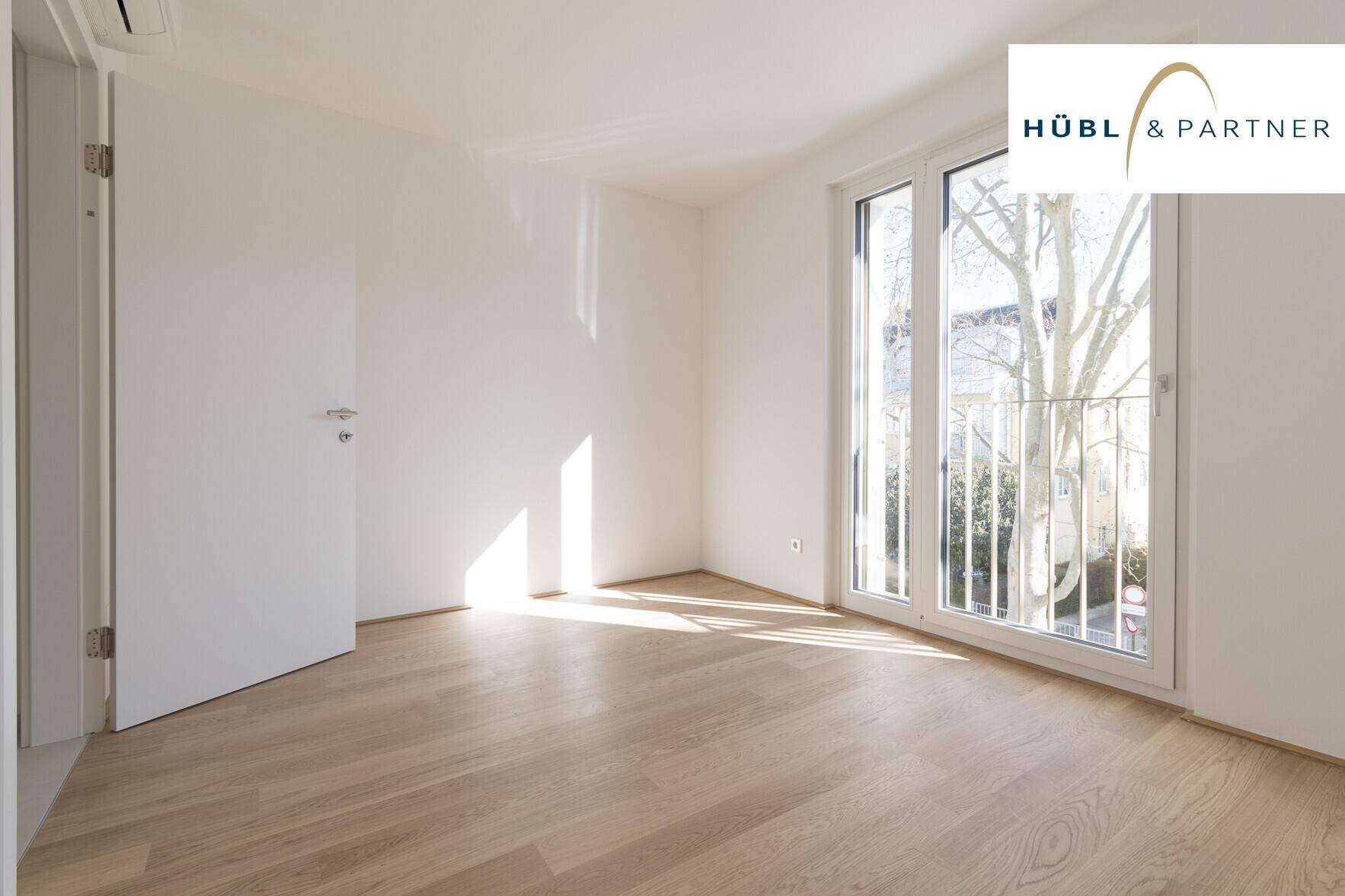 Helles Schlafzimmer mit Parkettboden und großem Fenster, das viel natürliches Licht hereinlässt.