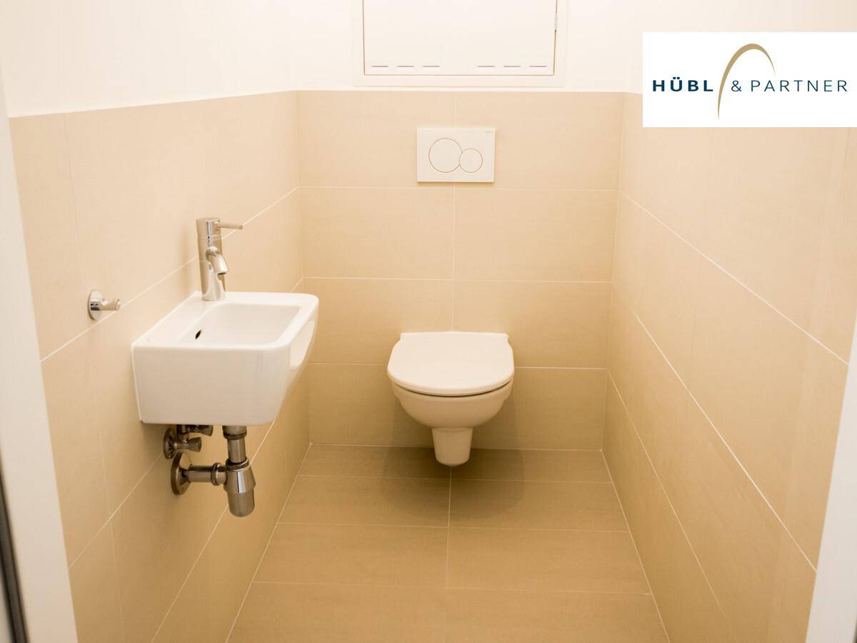 Kleines Gäste-WC mit wandhängender Toilette, kompaktem Waschbecken und hellen Fliesen.