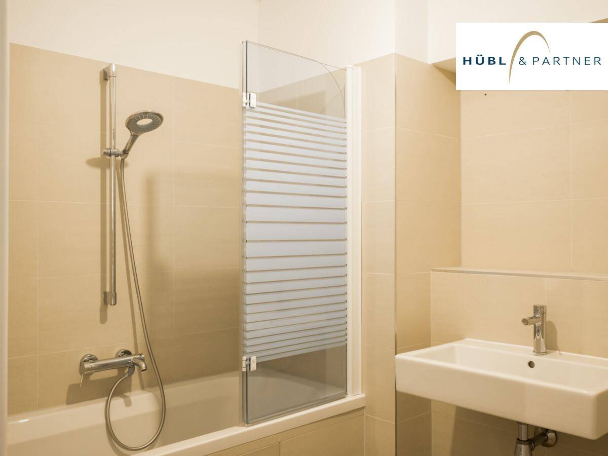 Badezimmer mit Badewanne, Duschvorrichtung, Waschbecken und hellen Fliesen an Wänden und Boden.
