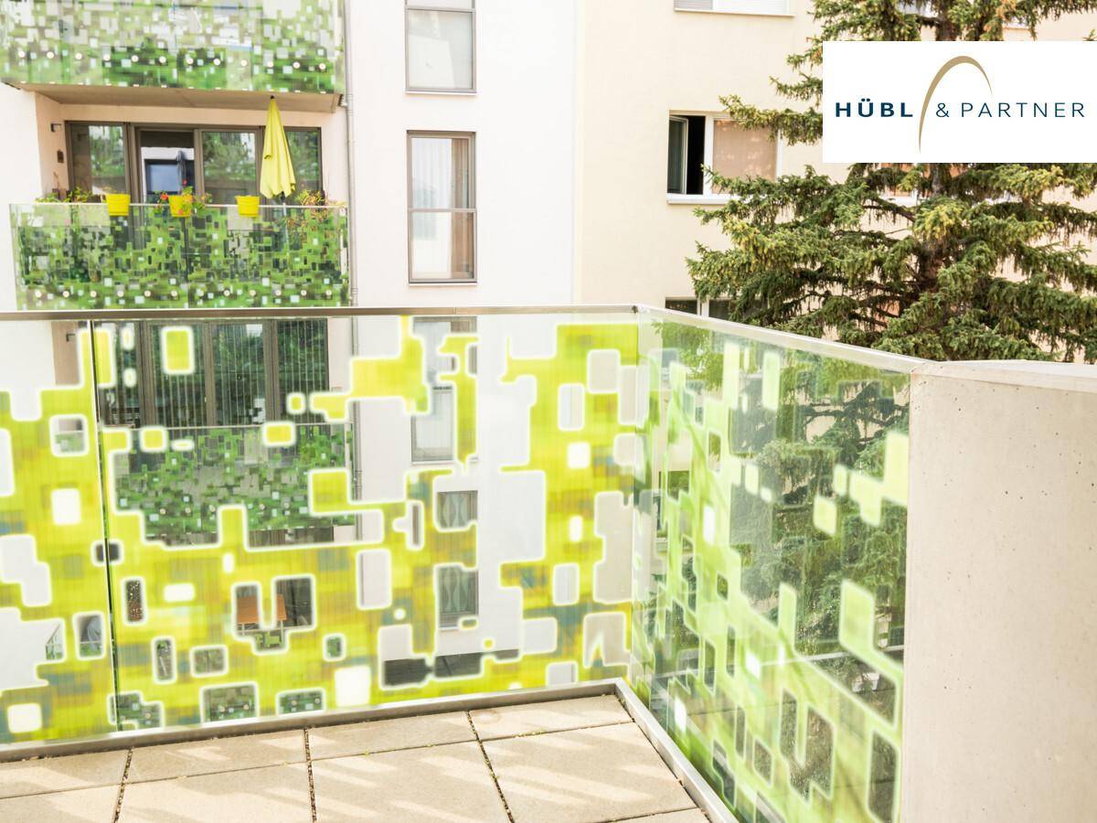 Balkon mit modernem, gemustertem Glasgeländer und Blick auf die umliegenden Gebäude und Bäume.