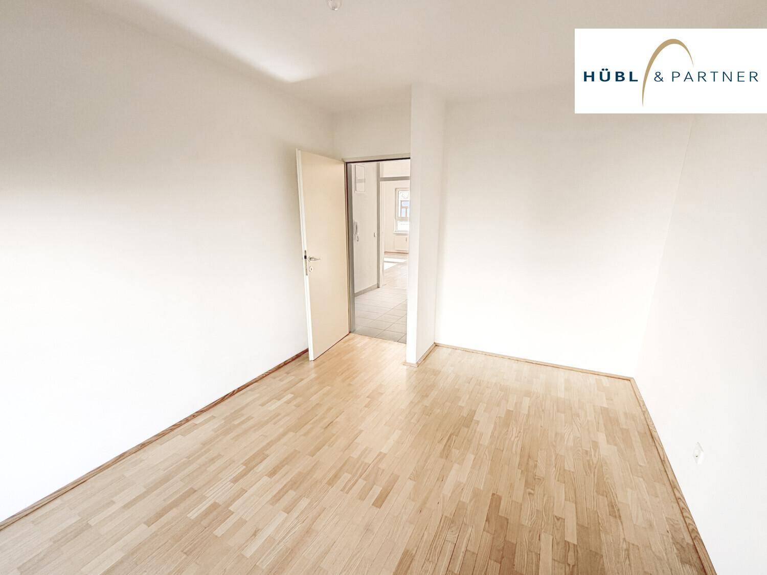 Helles, leeres Zimmer mit Parkettboden und Zugang zu weiteren Räumen, ideal als Schlafzimmer.