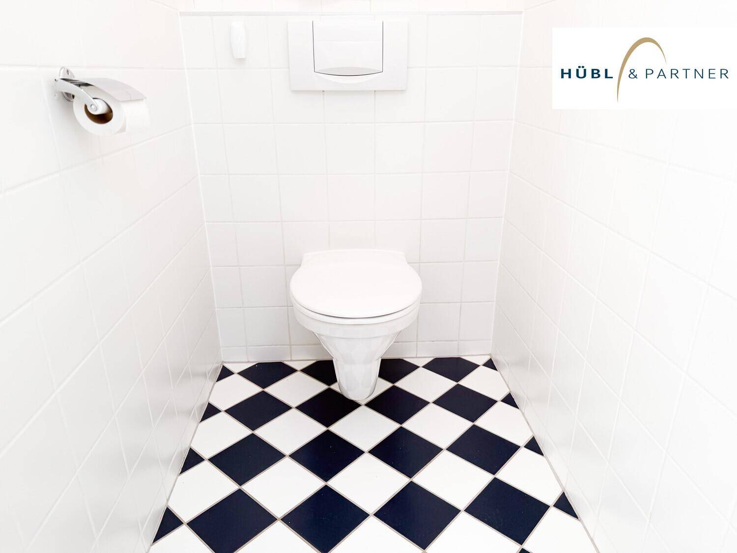 Separates WC mit weiß gefliesten Wänden und einem auffälligen schwarz-weiß karierten Boden.