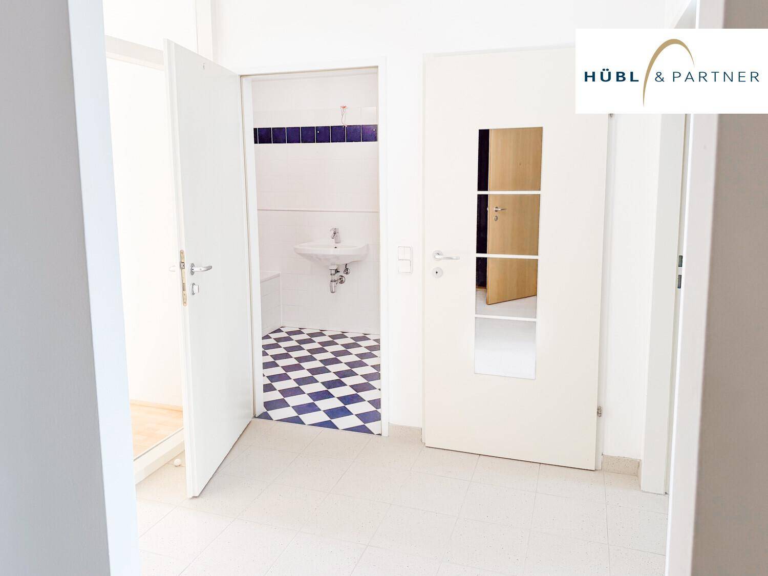 Heller Flur mit Blick in ein Badezimmer mit markantem schwarz-weiß kariertem Fliesenboden.