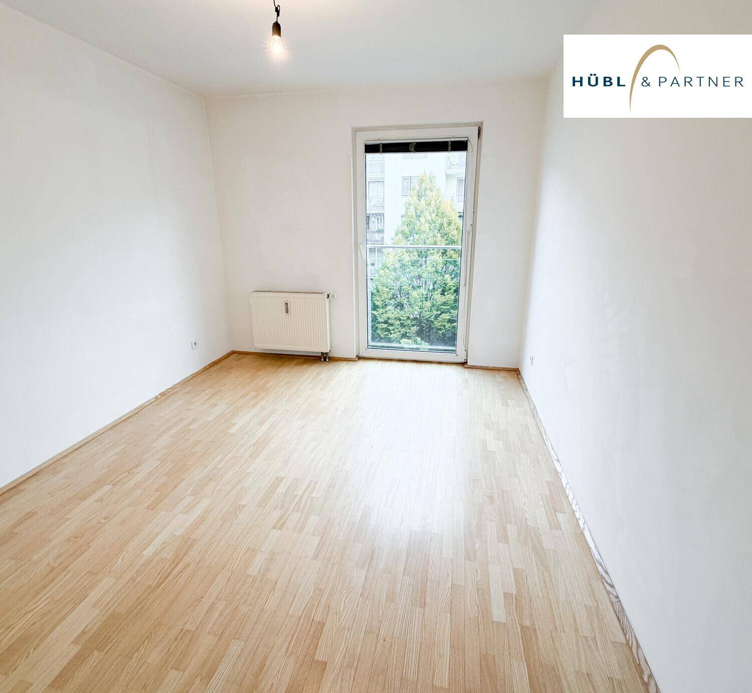 Helles Zimmer mit Parkettboden und großem Fenster, das einen Blick ins Grüne bietet.