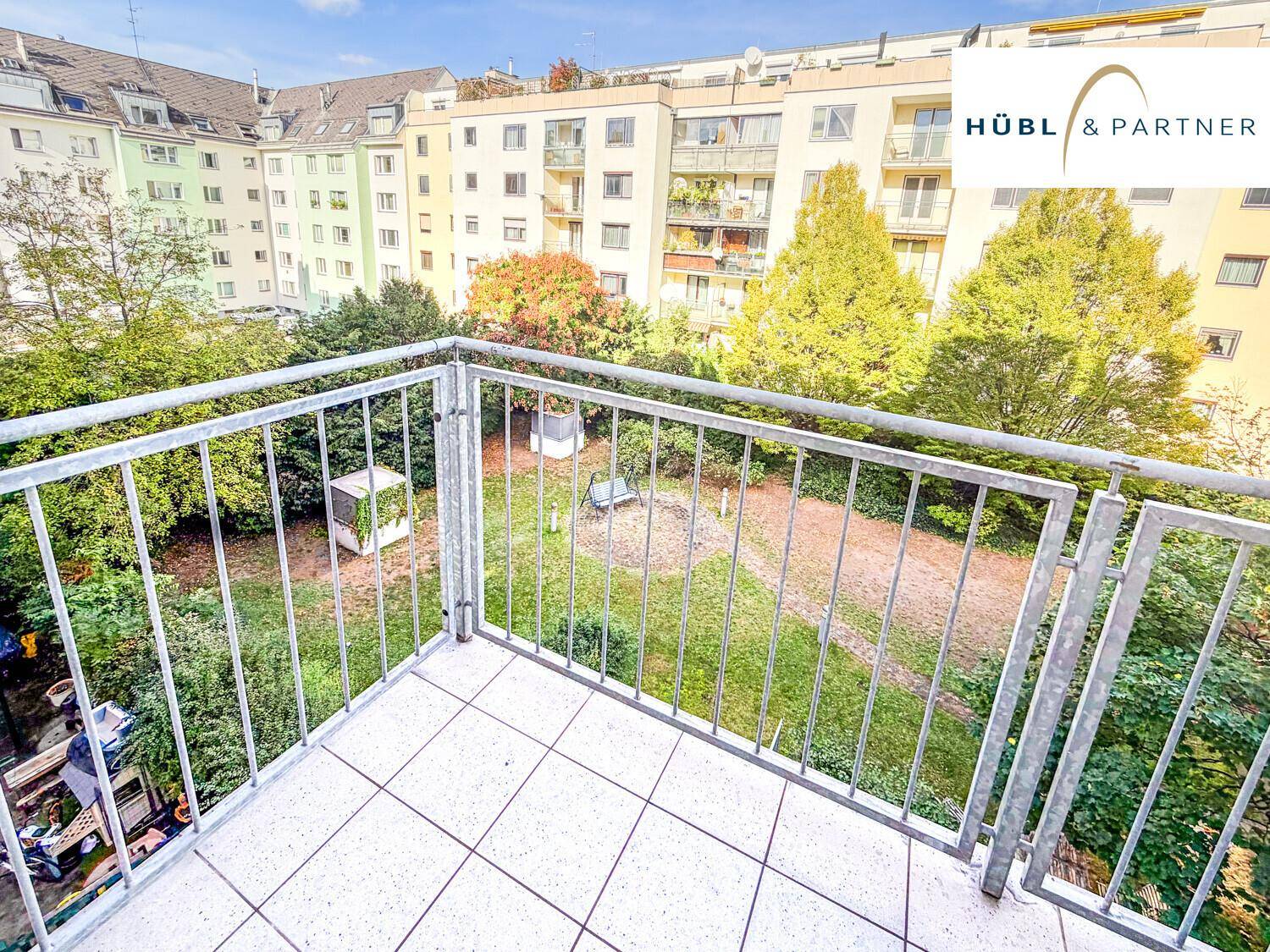 Balkon mit Metallgeländer und weitem Blick über den grünen Innenhof.