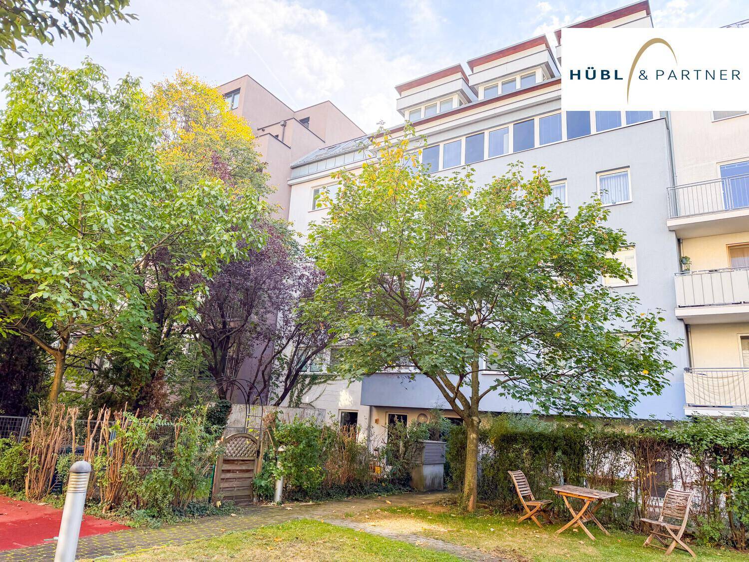 Grüner Gemeinschaftsgarten mit Bäumen und Sitzgelegenheiten hinter dem Gebäude.
