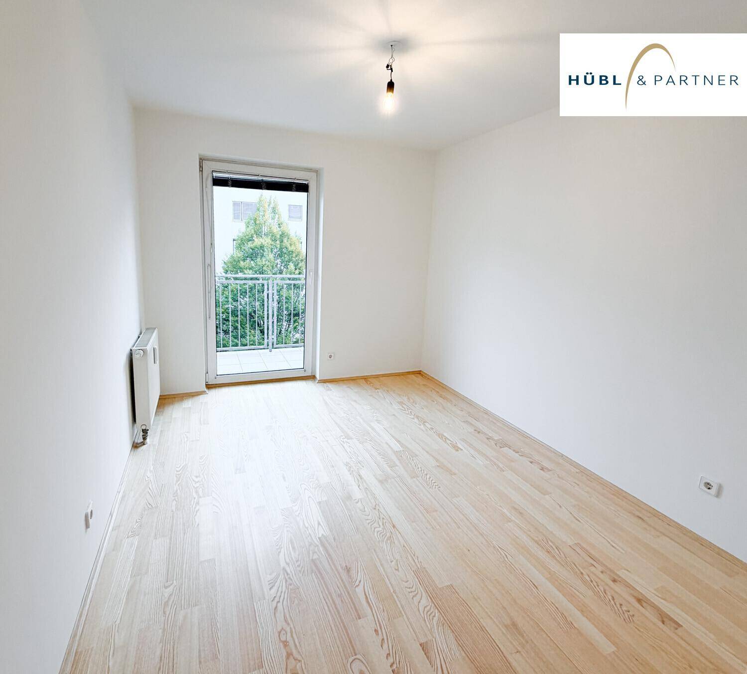 Leeres Zimmer mit Parkettboden und Zugang zu einem kleinen Balkon oder einer französischen Balkontür.